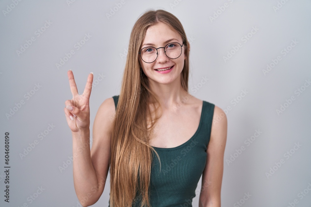 Young caucasian woman standing over white background showing and pointing up with fingers number two while smiling confident and happy. Young caucasian woman standing over white background showing and pointing up with fingers number two while smiling confident and happy.