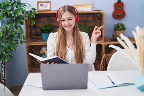 Young caucasian woman studying using computer laptop smiling happy pointing with hand and finger to the side