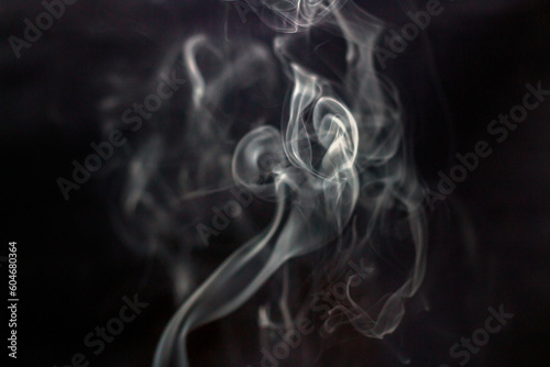 A lot of white smoke from incense curls beautifully up in the air on a black background close-up