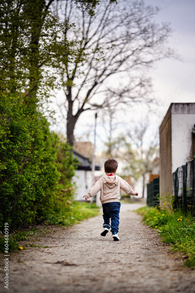 Little toddler boy runs the earth road in spring in hoodie and jeans. Kid run away, from the back Little toddler boy runs the earth road in spring in hoodie and jeans. Kid run away, from the back