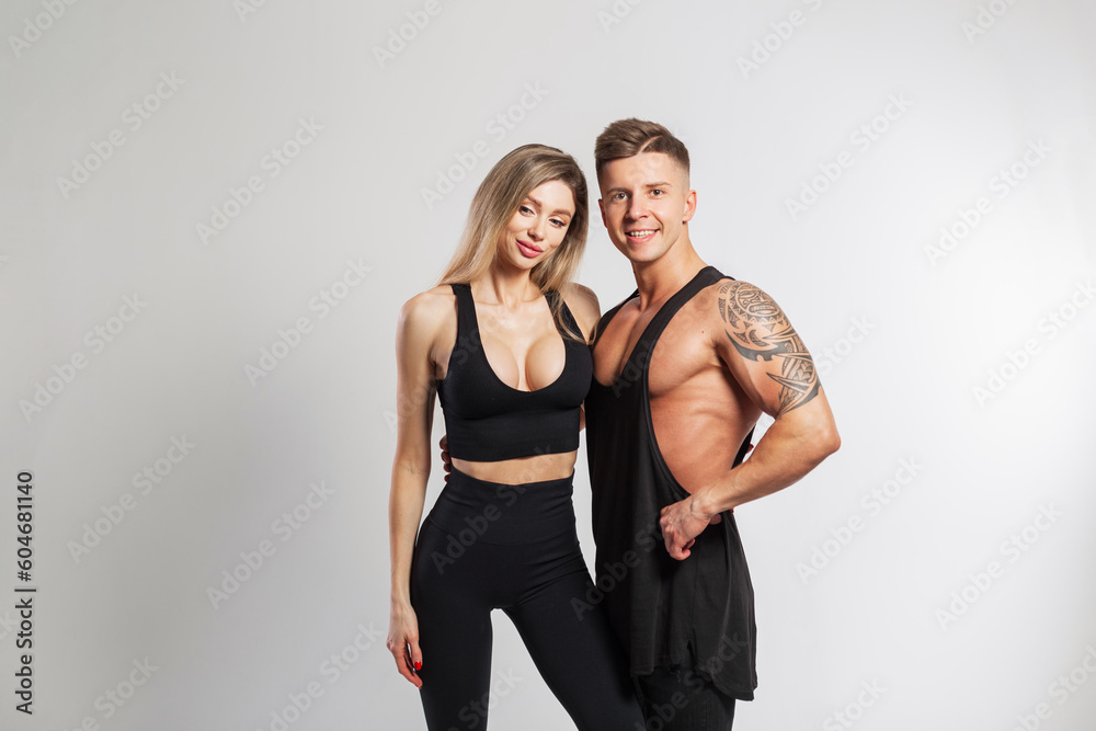 Beautiful sports couple in the studio. Beautiful young fitness girl and handsome strong muscular man in fashionable black sportswear on a white background