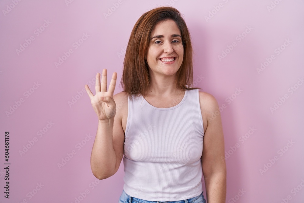 Brunette woman standing over pink background showing and pointing up with fingers number four while smiling confident and happy. Brunette woman standing over pink background showing and pointing up with fingers number four while smiling confident and happy.