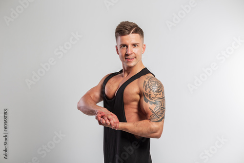 Cool strong athletic fit man with hairstyle in black tank top showing biceps with tattoo on white background in studio