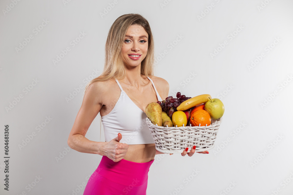 Happy beautiful young sports fitness girl with a smile in sportswear holding a fruit basket on a white background. Healthy food and diet Happy beautiful young sports fitness girl with a smile in sportswear holding a fruit basket on a white background. Healthy food and diet