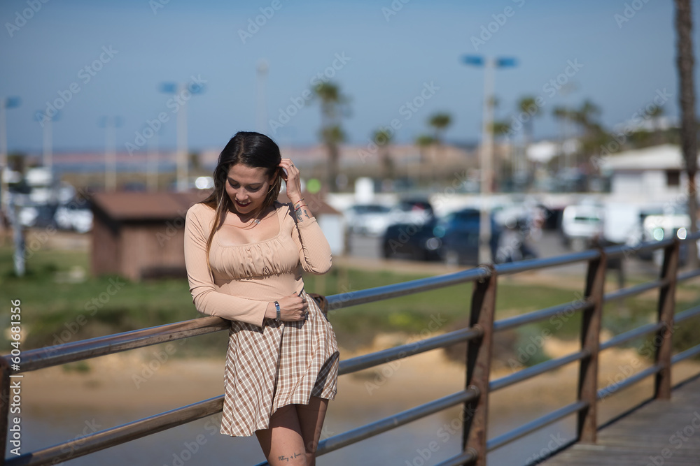 Attractive young woman with blue eyes, sweater and plaid skirt, leaning on the railing of a bridge, relaxed and happy. Concept relax, tranquility, peace.
