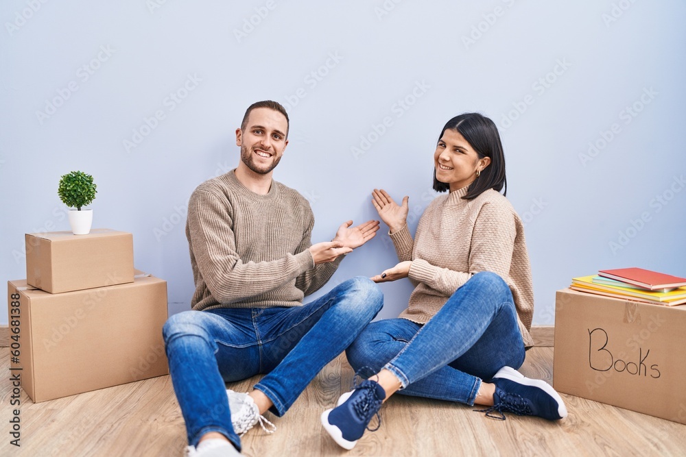 Young couple moving to a new home inviting to enter smiling natural with open hand Young couple moving to a new home inviting to enter smiling natural with open hand