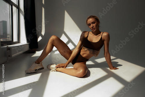 Motivated young lady exercising by posing in a bright studio. Fitness woman exercising in dark sportswear. Panorama, full-length plan