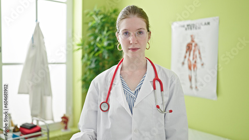 Young blonde woman doctor standing with serious expression at clinic