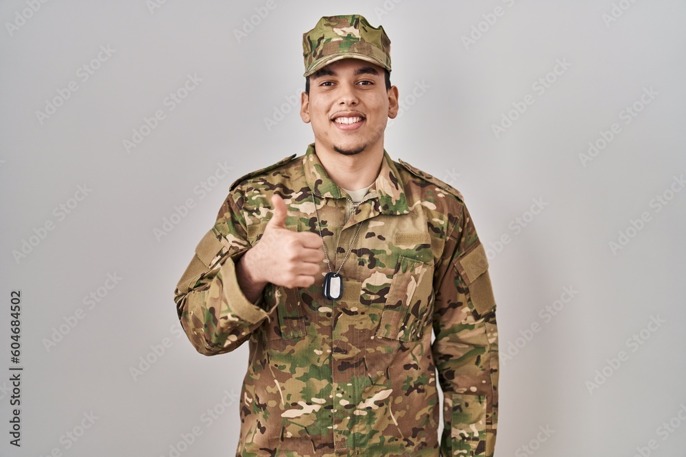 Young arab man wearing camouflage army uniform doing happy thumbs up gesture with hand. approving expression looking at the camera showing success.