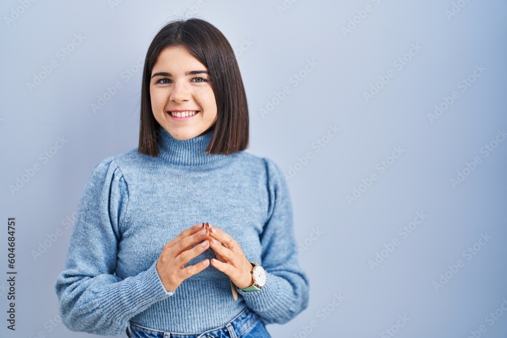 Young hispanic woman standing over blue background hands together and fingers crossed smiling relaxed and cheerful. success and optimistic Young hispanic woman standing over blue background hands together and fingers crossed smiling relaxed and cheerful. success and optimistic