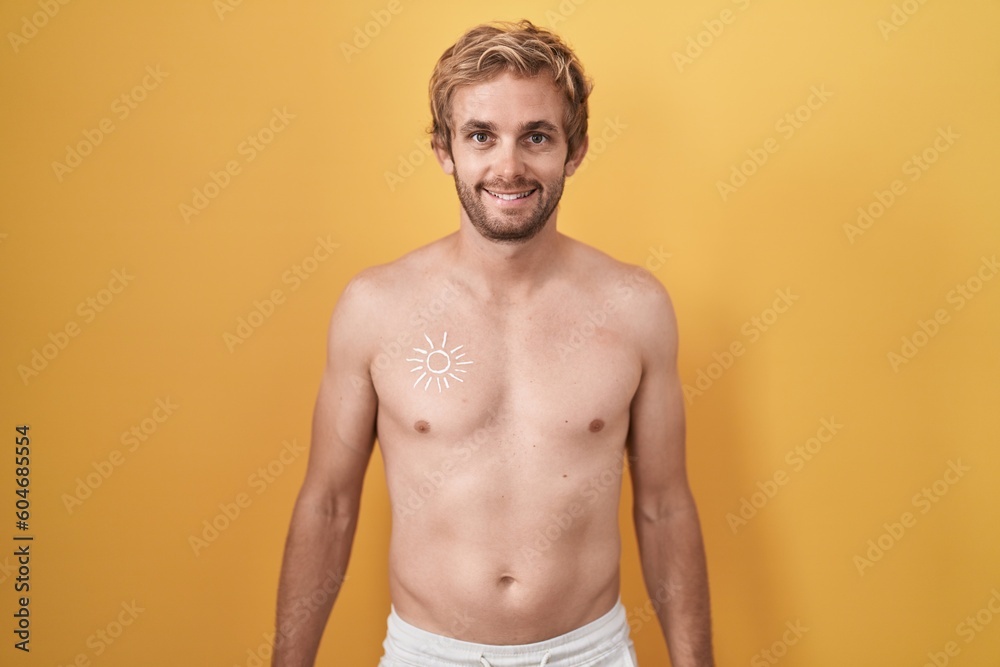 Caucasian man standing shirtless wearing sun screen with a happy and cool smile on face. lucky person.