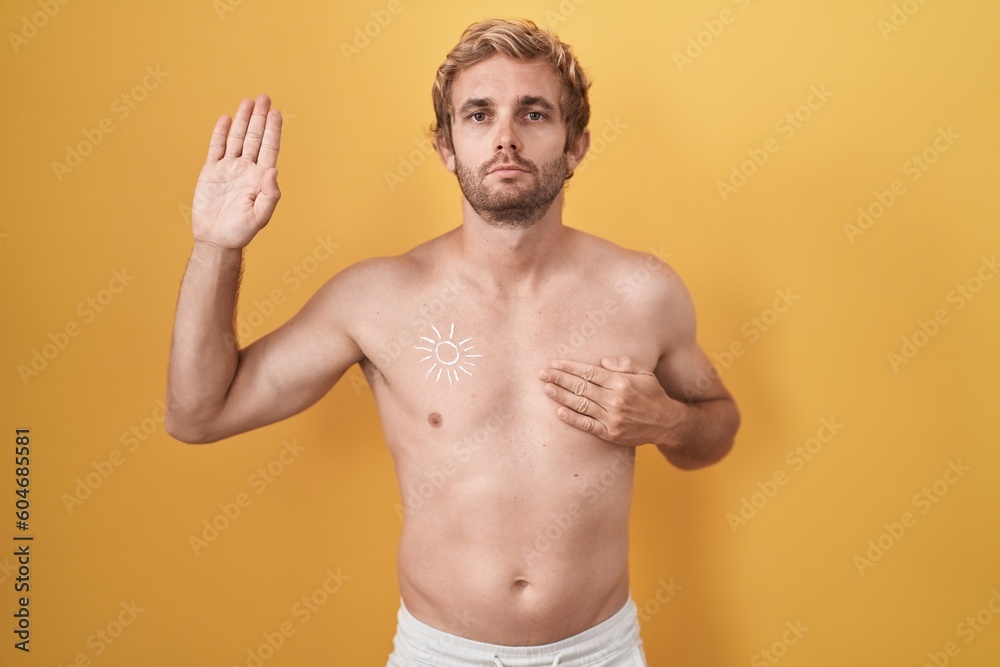 Fototapeta premium Caucasian man standing shirtless wearing sun screen swearing with hand on chest and open palm, making a loyalty promise oath