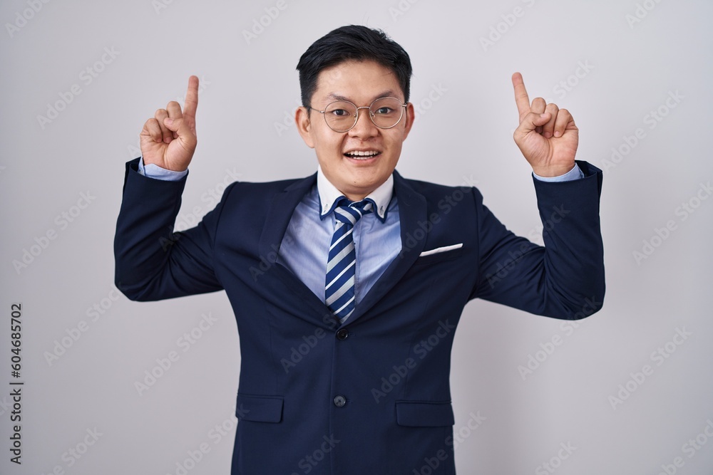 Young asian man wearing business suit and tie smiling amazed and surprised and pointing up with fingers and raised arms. Young asian man wearing business suit and tie smiling amazed and surprised and pointing up with fingers and raised arms.