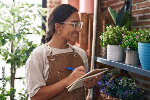 Young beautiful hispanic woman florist smiling confident writing on notebook at florist
