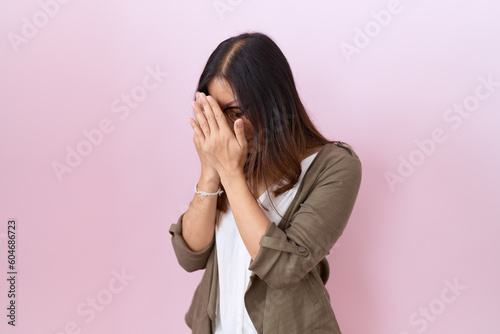 Middle age chinese woman wearing glasses over pink background with sad expression covering face with hands while crying. depression concept. © Krakenimages.com
