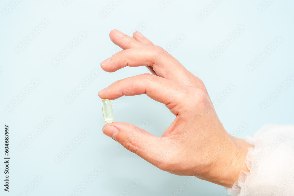 Doctor's hand holding a fish oil capsule (Omega 3) or pill isolated on light blue background Doctor's hand holding a fish oil capsule (Omega 3) or pill isolated on light blue background