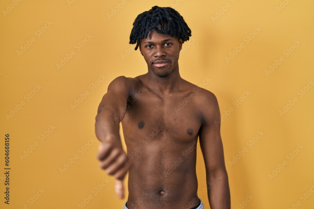 Fototapeta premium Young african man with dreadlocks standing shirtless looking unhappy and angry showing rejection and negative with thumbs down gesture. bad expression.