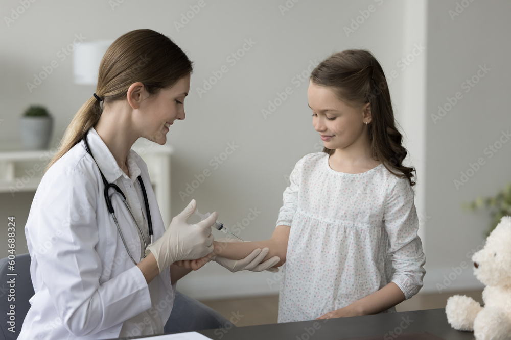 Fototapeta premium Caring female doc holds syringe gives injection from flu to girl kid patient, to prevent infection. Woman doctor vaccinate prick arm of little kid in modern clinic. Healthcare, medicine, immunization
