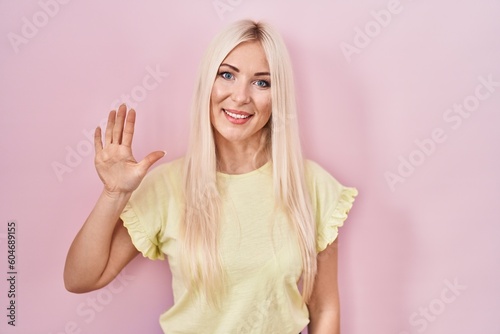 Caucasian woman standing over pink background showing and pointing up with fingers number five while smiling confident and happy.