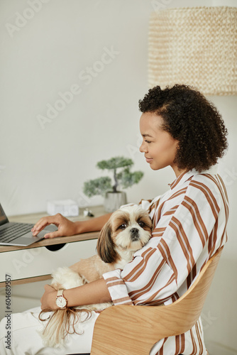 Side view portrait of black young woman working from home with pet dog sitting in lap
