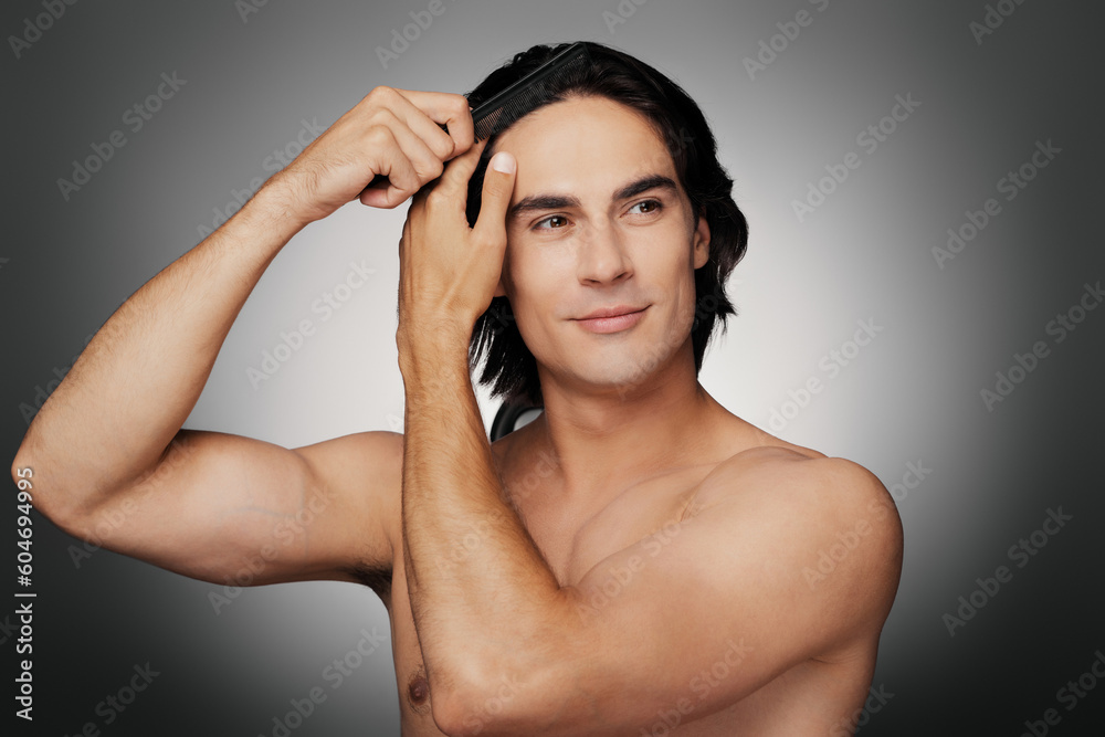 Fototapeta premium Handsome young shirtless man brushing his hair against grey background