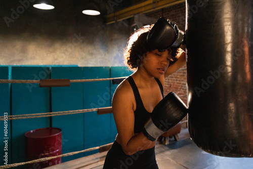 Women self defense girl power. African american woman fighter resting after fight training on boxing ring. Girl tired after punching boxing bag. Training day in gym. Strength fit body workout training © Юлия Завалишина