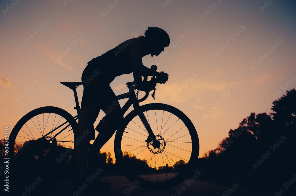 Fototapeta premium Silhouette of a woman riding a bike during a sport cycling race on a sunset