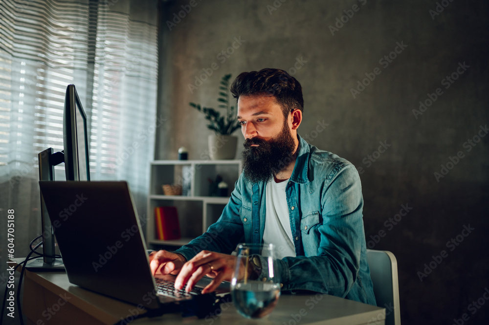 An operating data security worker is working from his darkened home office remotely. An operating data security worker is working from his darkened home office remotely.