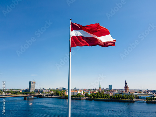 Huge Latvian flag flutters in the wind with Riga old town in the background in Latvia. Beautiful summer day.