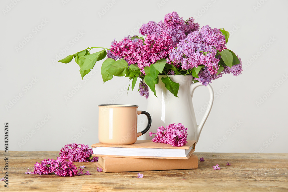Jug of beautiful lilac flowers with coffee and books on wooden table near white wall - obrazy, fototapety, plakaty 