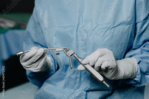 A surgeon in latex gloves and a blue uniform holds a special proctological instrument photo
