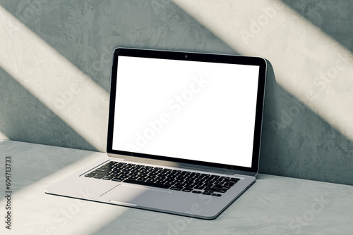 Perspective view on blank white modern laptop monitor with place for logo brand or web design on sunlit concrete wall background with shadows, advertising and marketing concept. 3D rendering, mock up