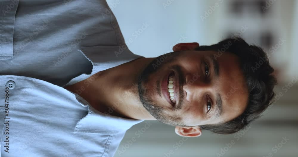Vertical view close up of handsome Indian business man in casual blue shirt posing standing alone indoor, smile look at camera. Millennial generation person, professional teacher or manager portrait Vertical view close up of handsome Indian business man in casual blue shirt posing standing alone indoor, smile look at camera. Millennial generation person, professional teacher or manager portrait
