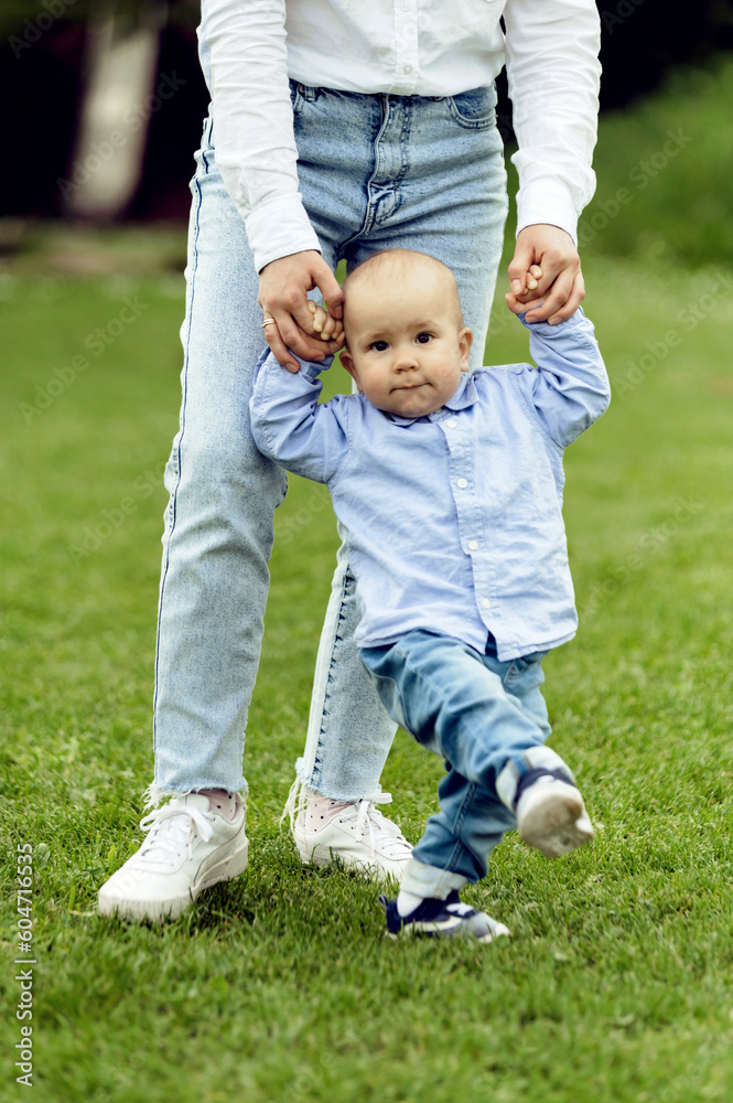 baby learns to walk holding mother's hands. walk with a little boy in nature. lovely one year old boy. child portrait baby learns to walk holding mother's hands. walk with a little boy in nature. lovely one year old boy. child portrait