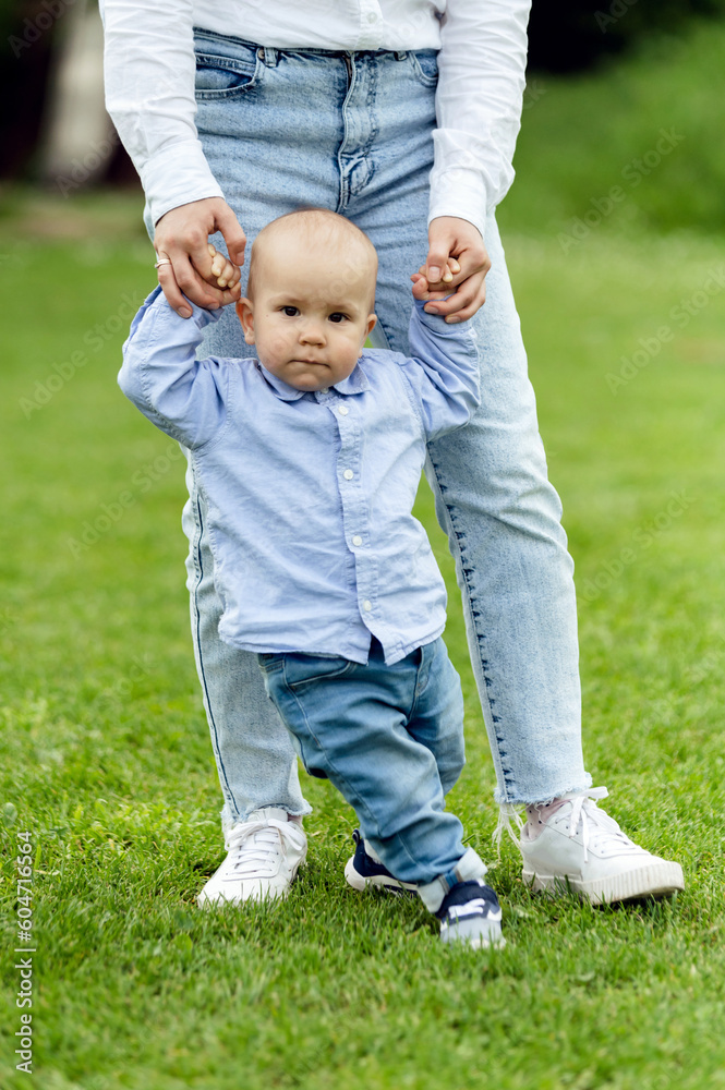 Fototapeta premium baby learns to walk holding mother's hands. walk with a little boy in nature. lovely one year old boy. child portrait