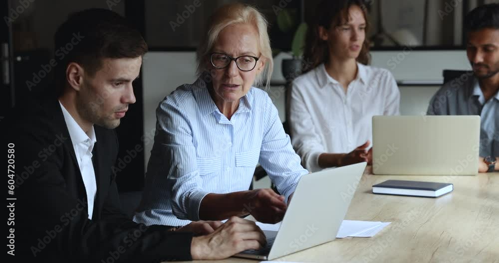 Mature female colleague helps to new employee with computer corporate software app in modern office, brainstorming ideas, explain online business services, share work moments, discuss online project Mature female colleague helps to new employee with computer corporate software app in modern office, brainstorming ideas, explain online business services, share work moments, discuss online project