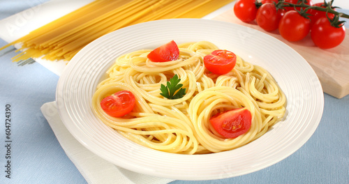 spaghetti on a plate. yellow noodles with tomatoes and parsley leaf. cooked pasta on a light background. Italian dish close-up. mediterranean cuisine. sunny day.