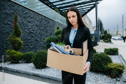 A stressed employee sits outside, holding a cardboard box after being fired from their job. Stressed Out Employee After Job Loss photo