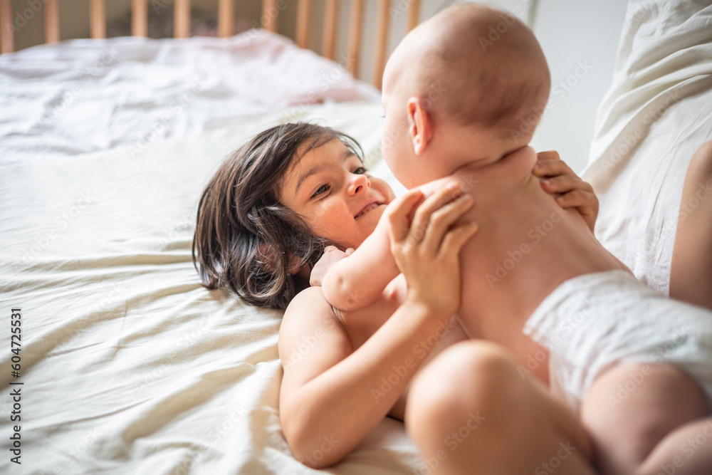 elder child playing with newborn lying on top on parents bed