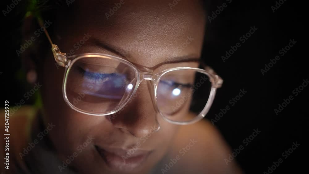 Close up of reflection of computer screen on the glasses of an African American hacker woman working on her laptop in the dark. Young people and security of computer networks and Internet. Close up of reflection of computer screen on the glasses of an African American hacker woman working on her laptop in the dark. Young people and security of computer networks and Internet.