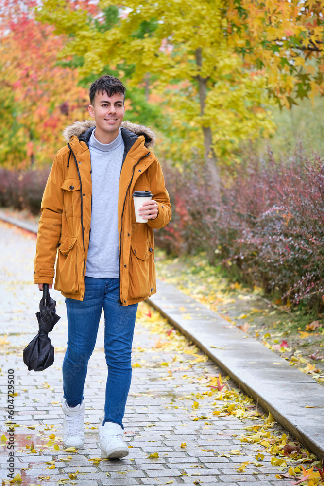 Portrait of a smiling young man holding cup of coffee and umbrella in a rainy autumn day at the street. Portrait of a smiling young man holding cup of coffee and umbrella in a rainy autumn day at the street.