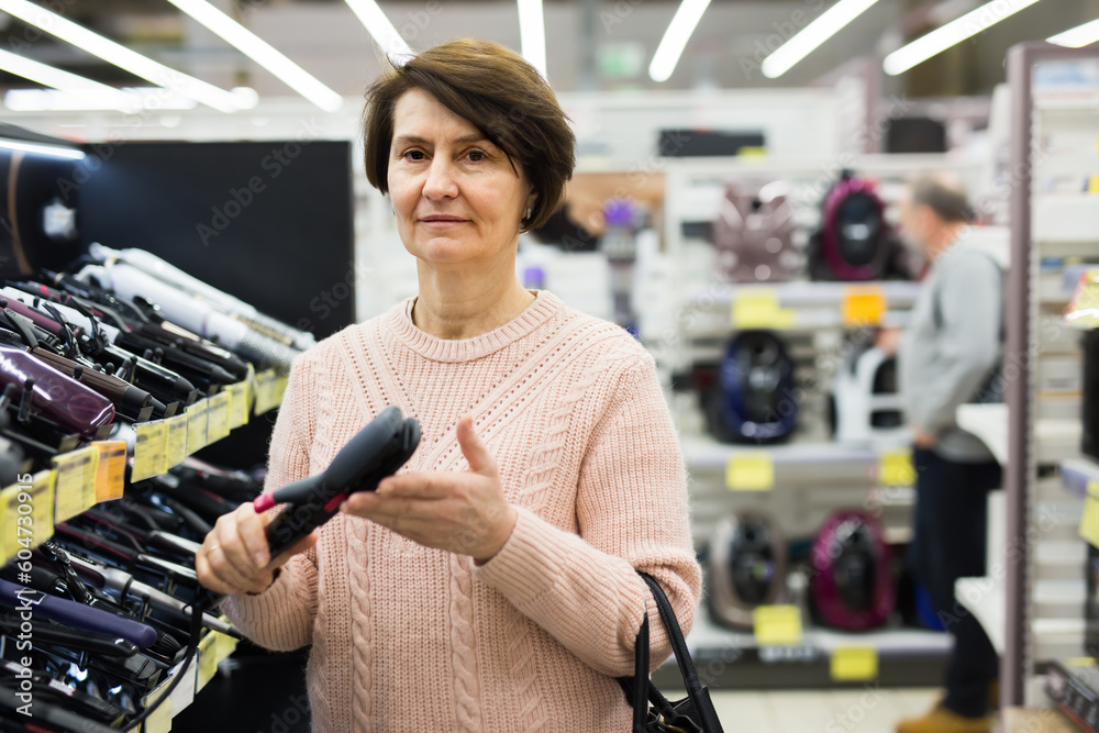 Portrait of a European woman choosing an electric styler near the shelves with goods in an electronics and household .appliances store