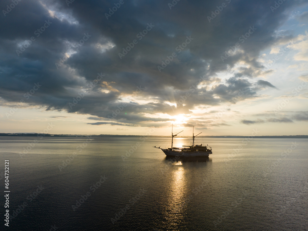 A tranquil sunrise illuminates a Phinisi schooner on the Pacific Ocean not far from Fak Fak, West Papua, Indonesia. This remote tropical area is home to extraordinary marine biodiversity.