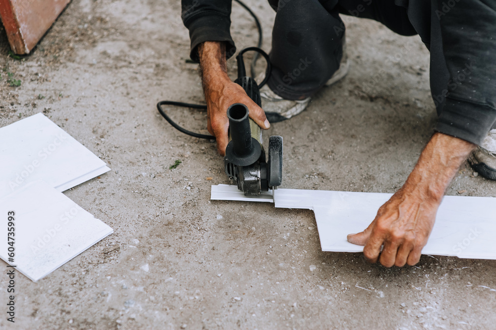 A man, a worker, cuts off plastic material for insulation with a grinder, an electric cutter. A man, a worker, cuts off plastic material for insulation with a grinder, an electric cutter.