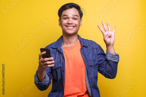 Young Asian man wearing casual clothes showing and pointing up with fingers number four while smiling confident and happy and holding smartphone.  photo