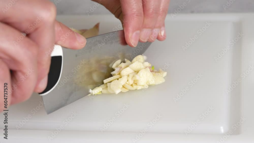 The chef chopping garlic on a white plastic cutting board, close-up view, preparation process The chef chopping garlic on a white plastic cutting board, close-up view, preparation process