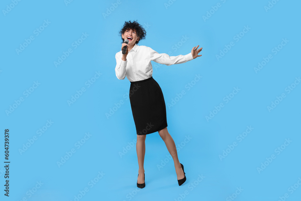 Beautiful young woman with microphone singing on light blue background Beautiful young woman with microphone singing on light blue background