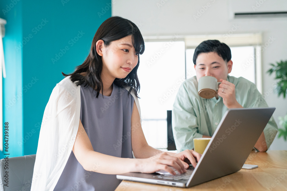 自宅でリモートワークをする妻と彼女を見守る夫 自宅でリモートワークをする妻と彼女を見守る夫