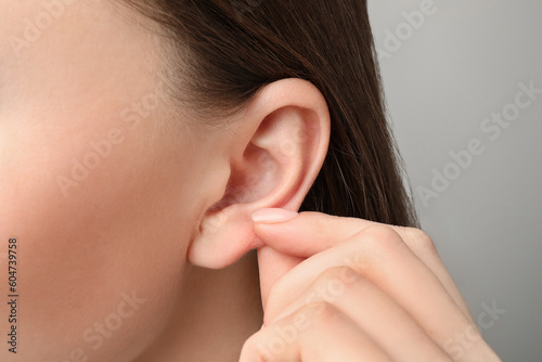 Woman touching her ear on light grey background, closeup photo