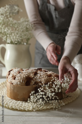Woman decorating delicious Italian Easter dove cake (traditional Colomba di Pasqua) with flowers at white wooden table, closeup